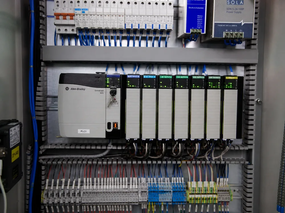 Open electrical control cabinet with DIN-rail PLC modules, I/O cards, and wiring